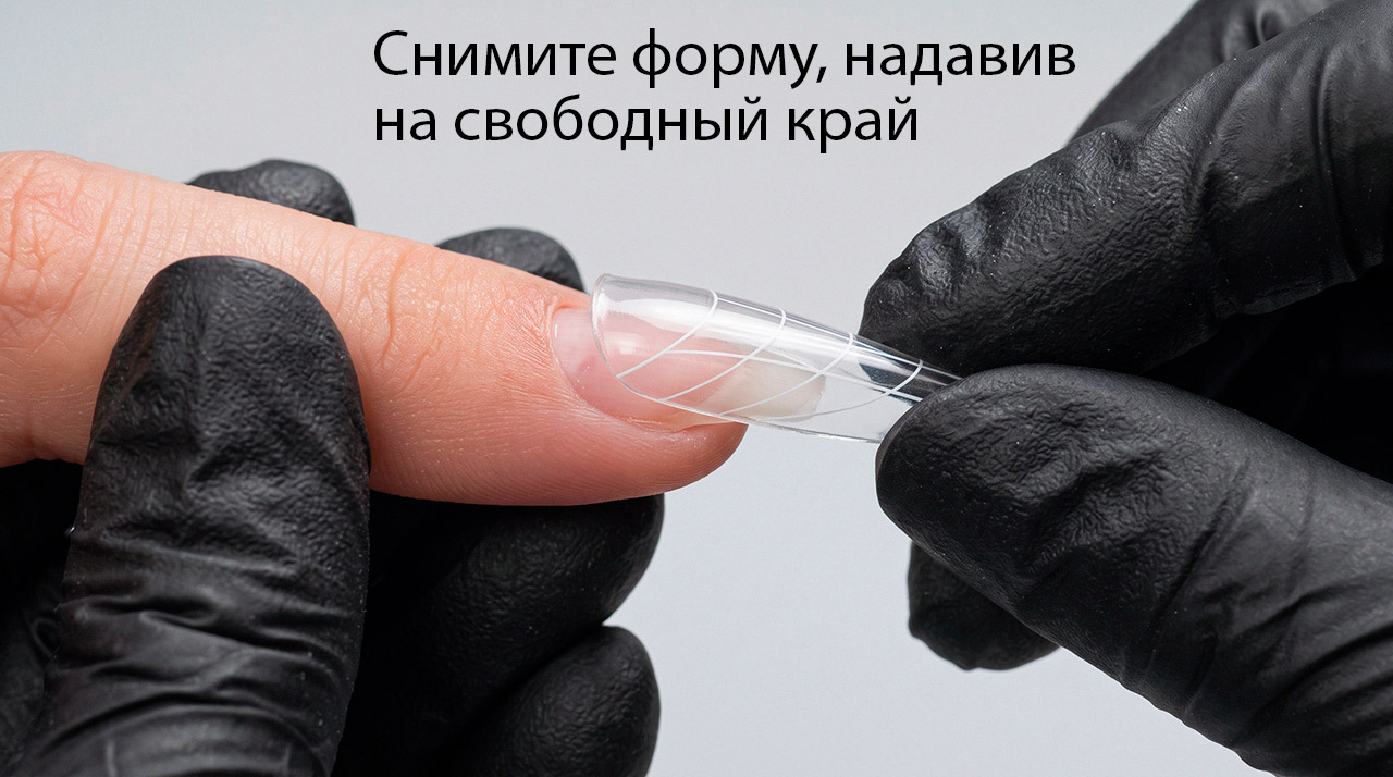 Мастер снимает пластиковую верхнюю форму со смоделированного ногтя, надавливая на ее свободный край
